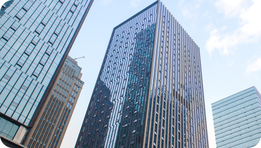 An upward-looking shot of modern glass-and-steel skyscrapers against a bright, lightly clouded sky.