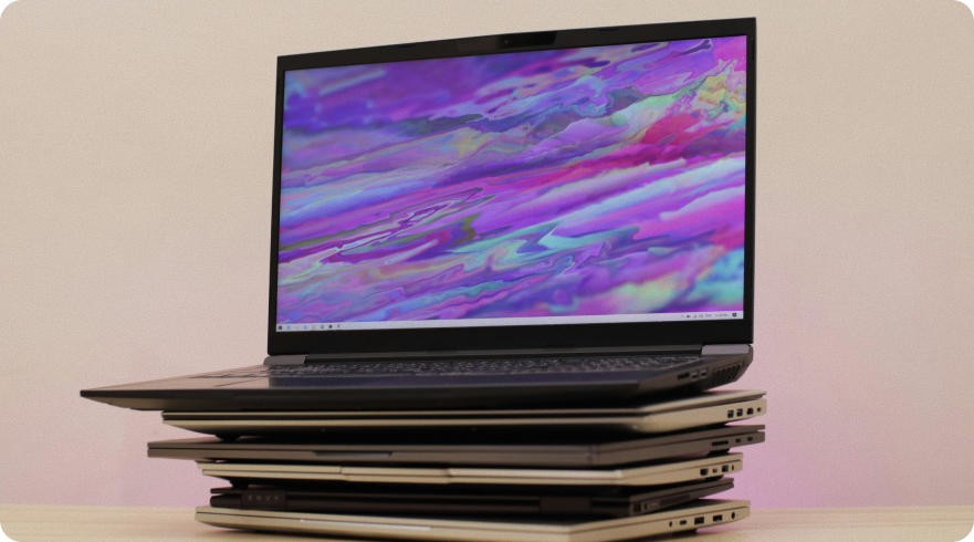 Pile of old laptops stacked on top of each other, with the top laptop open and displaying a colorful, abstract wallpaper. The image illustrates the concept of **IT sustainability** and the **device life cycle**, highlighting the need for responsible e-waste management.